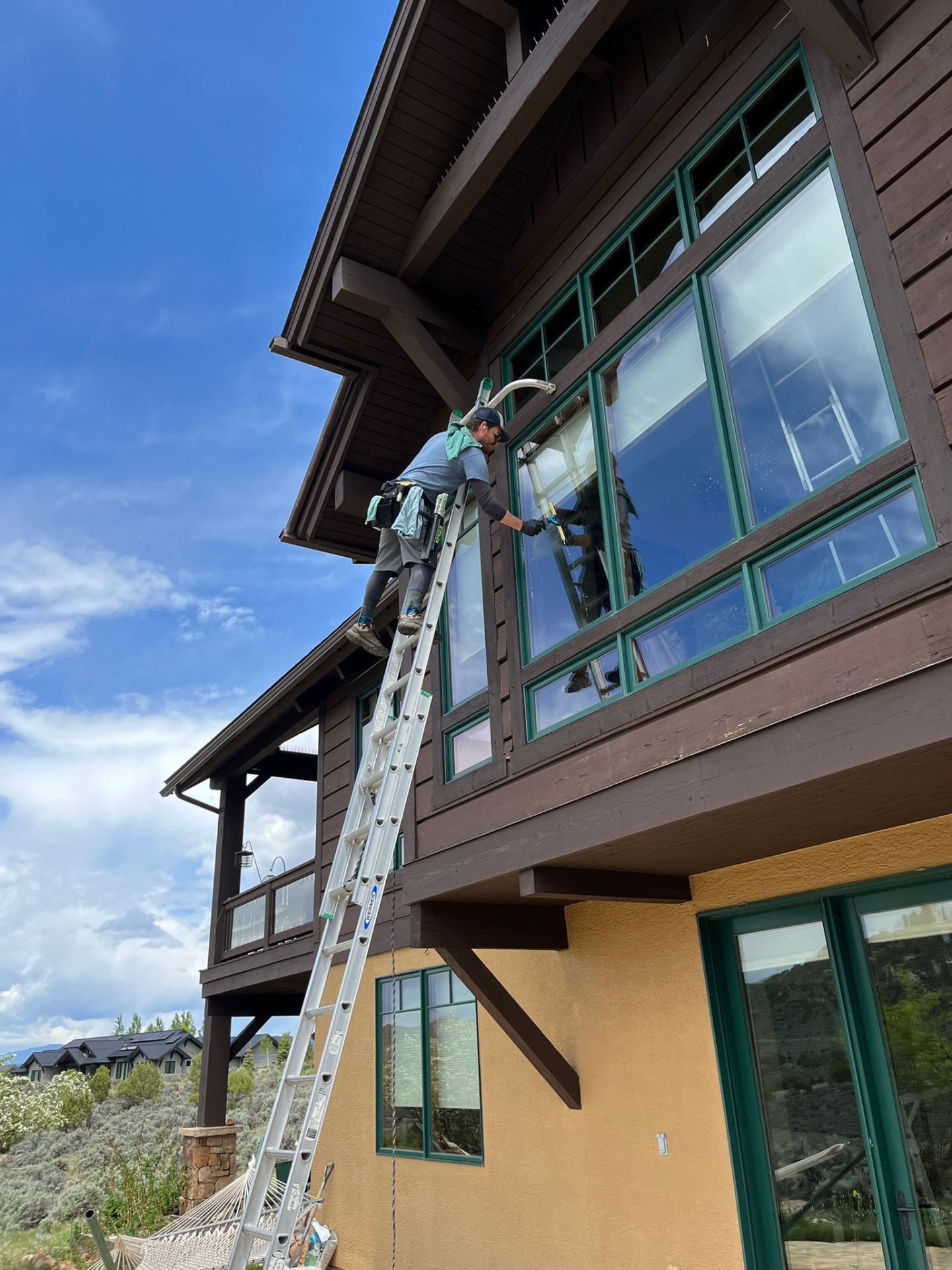 Residential window cleaning on the second-story windows of a brown mountain-style home in Eagle, Colorado under a blue sky