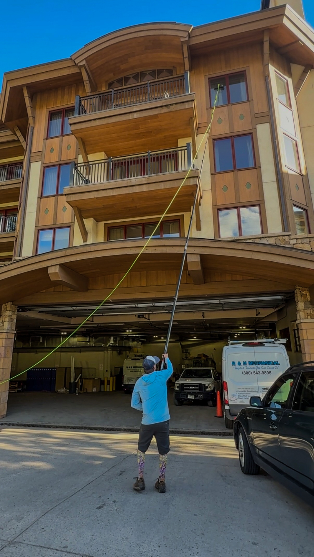Professional window cleaner using a water-fed pole to clean upper-story exterior windows on a timber-and-stone home in Vail, Colorado