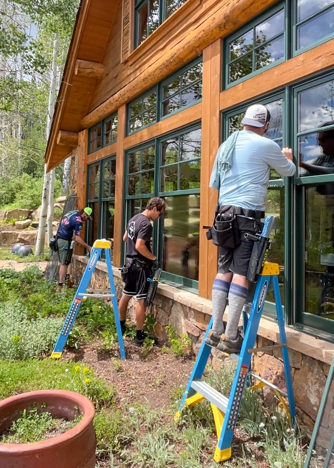 Residential window cleaning crew on ladders washing tall windows on a timber and log custom home in Cordillera, Edwards, Colorado