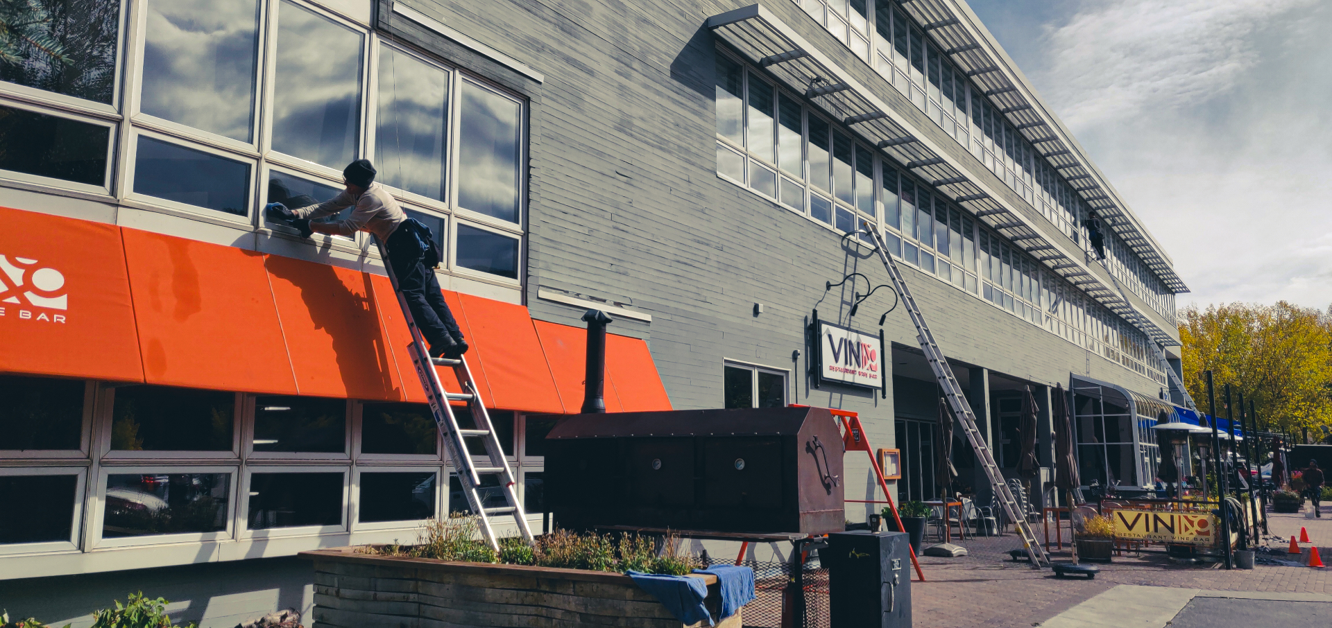 Professional window cleaner on a ladder washing second-story storefront windows on a commercial building in Avon, Colorado